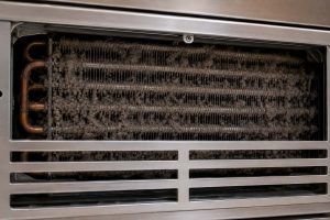 Close-up of a dust-clogged Sub-Zero condenser coil behind the upper grille