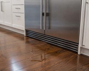 Puddle of water on a hardwood floor in front of a stainless steel Sub-Zero built-in refrigerator